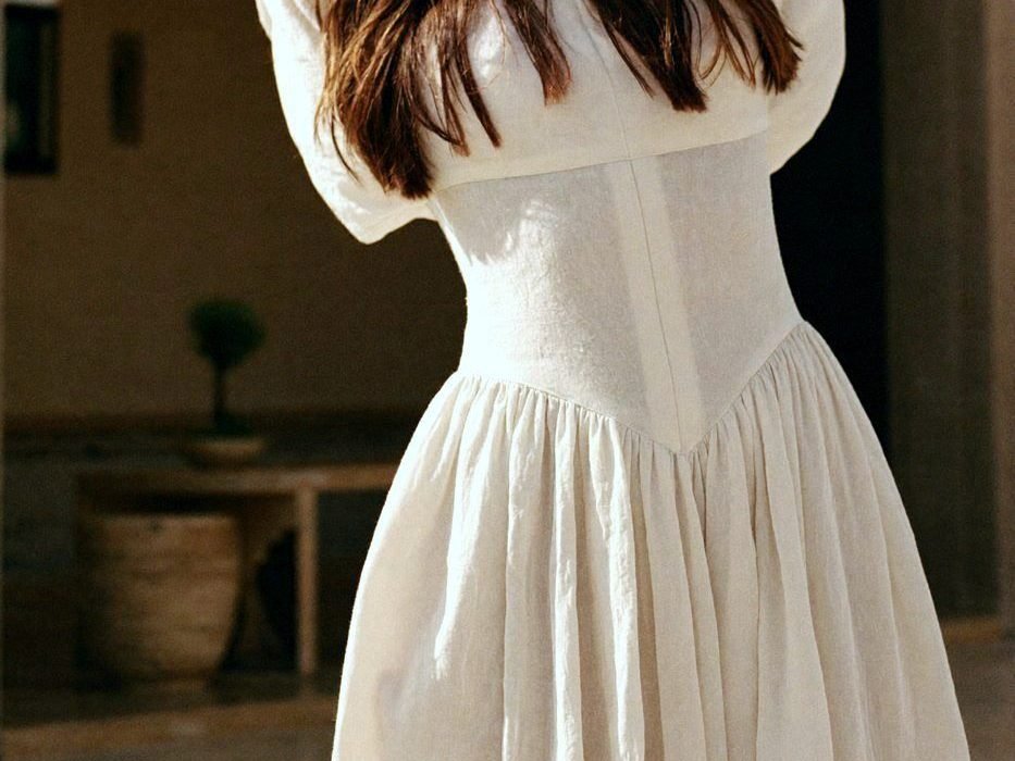A woman in a white dress, seen from behind, in a calm morning room