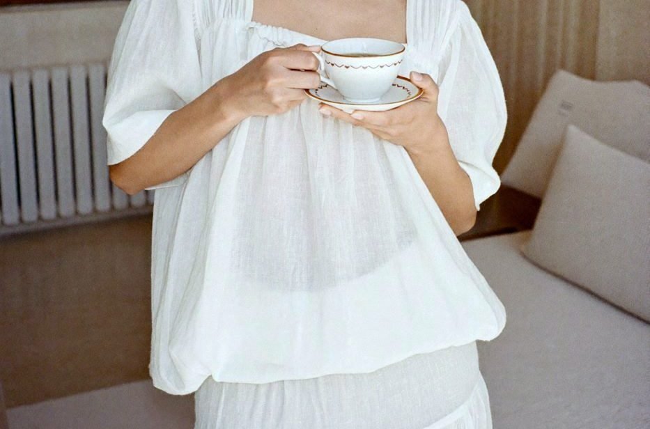 Hands holding a warm cup of tea against a white linen top